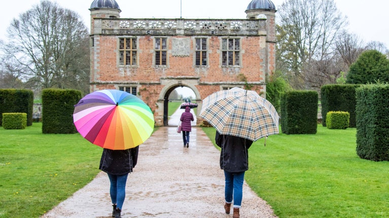 Two visitors with umbrellas are facing Charlecote's Gatehouse